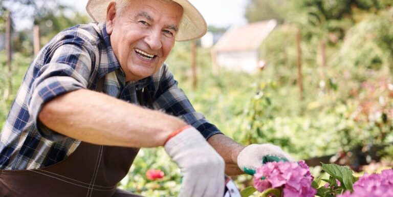 Elderly Man Gardening and Smiling While Tending Flowers at an Assisted Living Facility